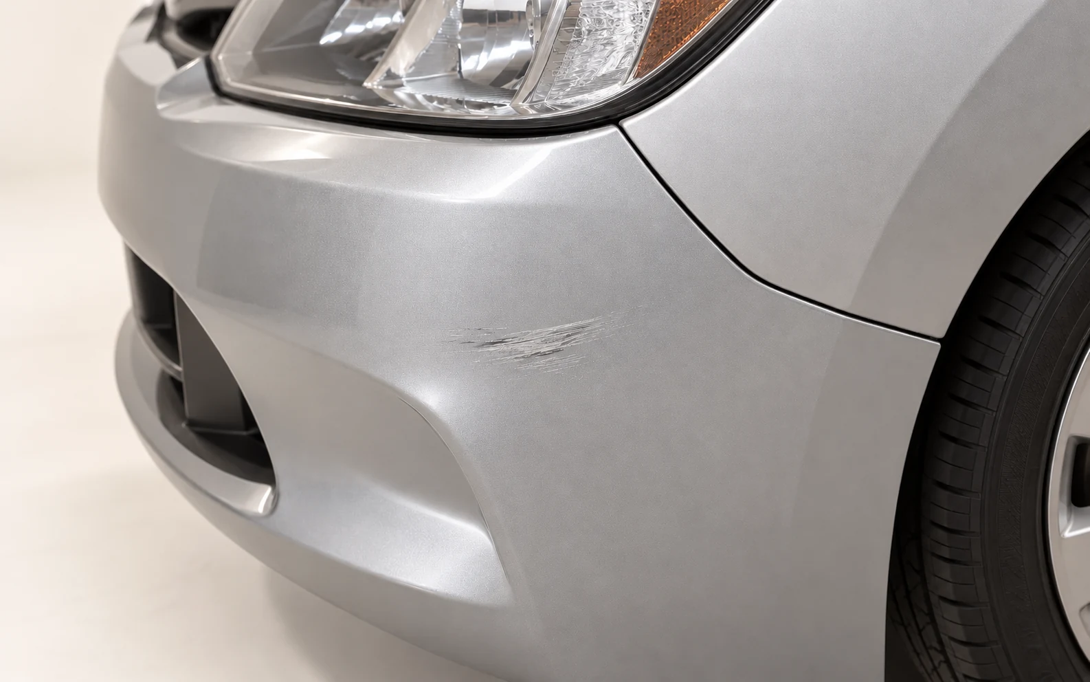 Conceptual silver bumper and matching silver fender beside a headlamp, with a localized surface scuff below the panel seam.